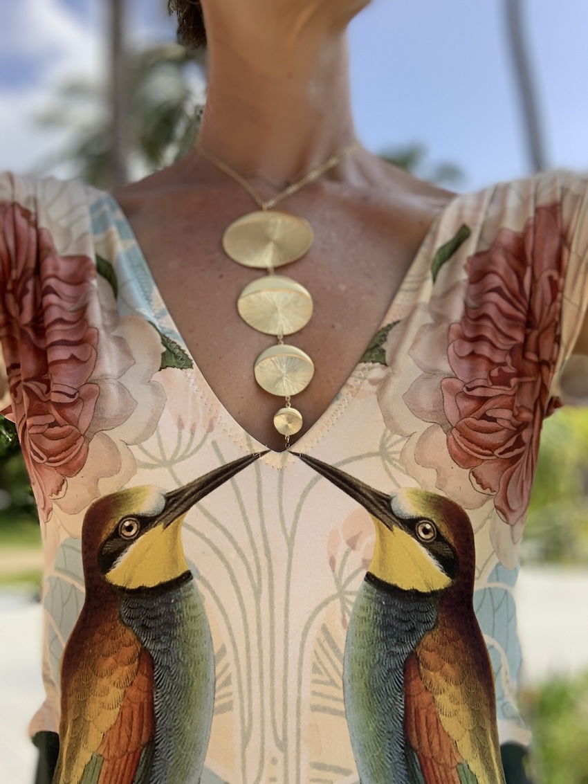Collier doré artisanal porté avec une robe illustrée de motifs floraux et d’oiseaux.